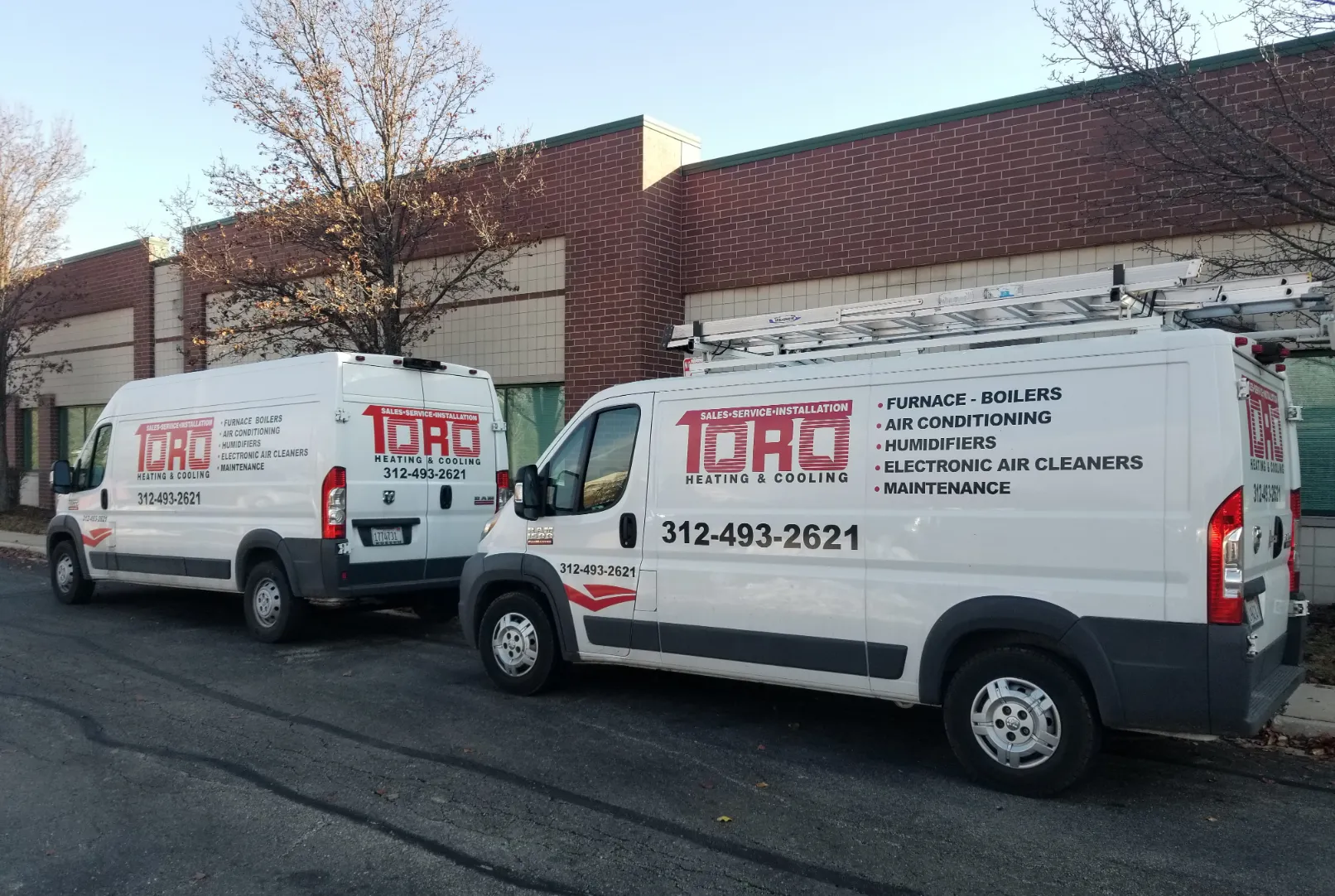 Two TORO Heating & Cooling service vans parked outside a brick building.